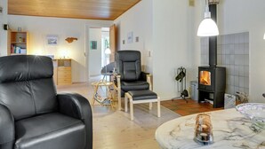 Un salon moderne avec un canapé en cuir noir, un plafond en bois, un fauteuil noir, une table basse en marbre et un poêle à bois.