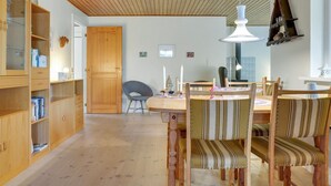 Une pièce chaleureuse avec un plancher en bois, une table de salle à manger ronde entourée de chaises, une bibliothèque en bois et un plafond avec des poutres apparentes.