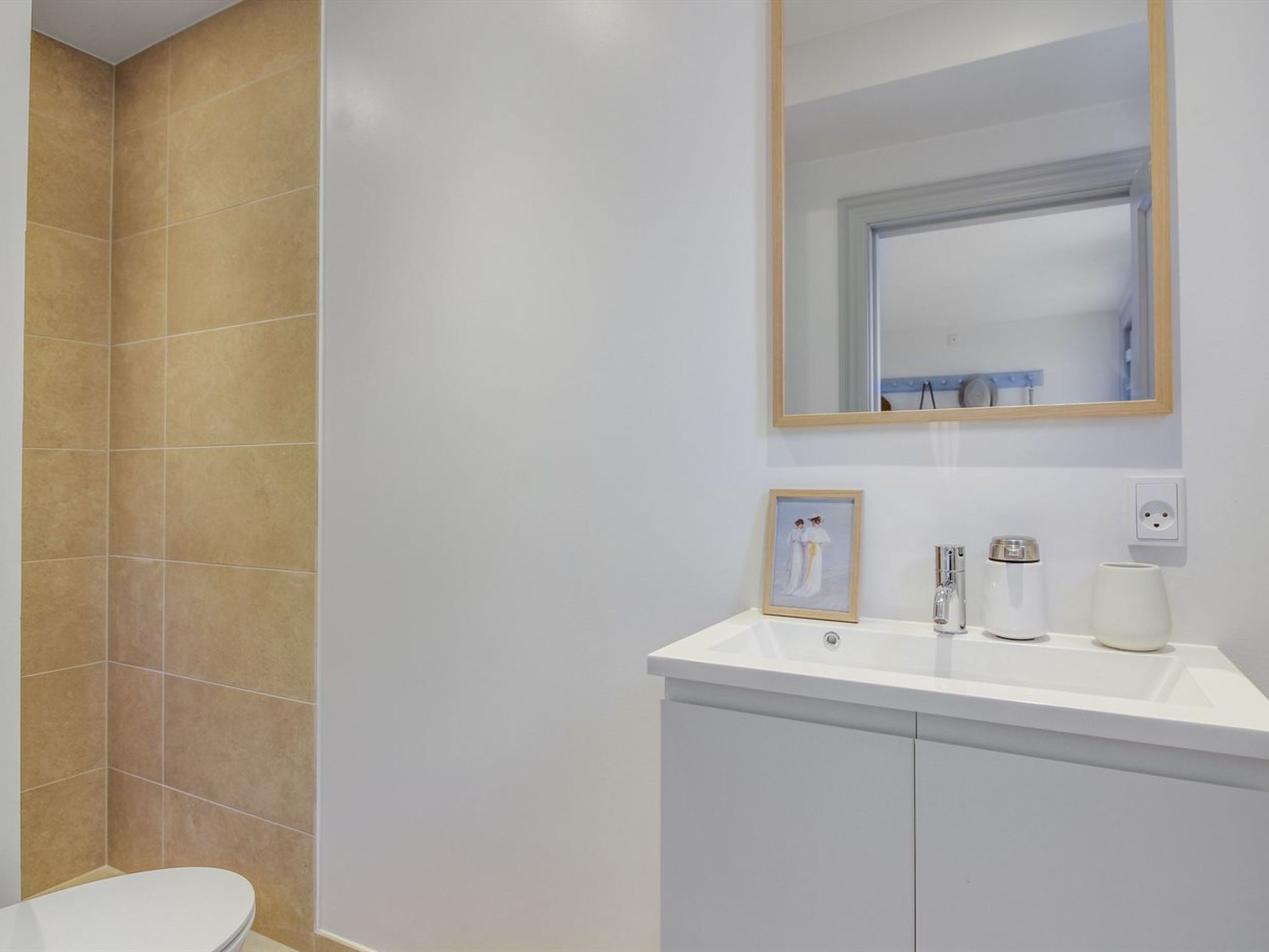 Une salle de bain avec un lavabo blanc, un miroir et un tableau encadré au mur.