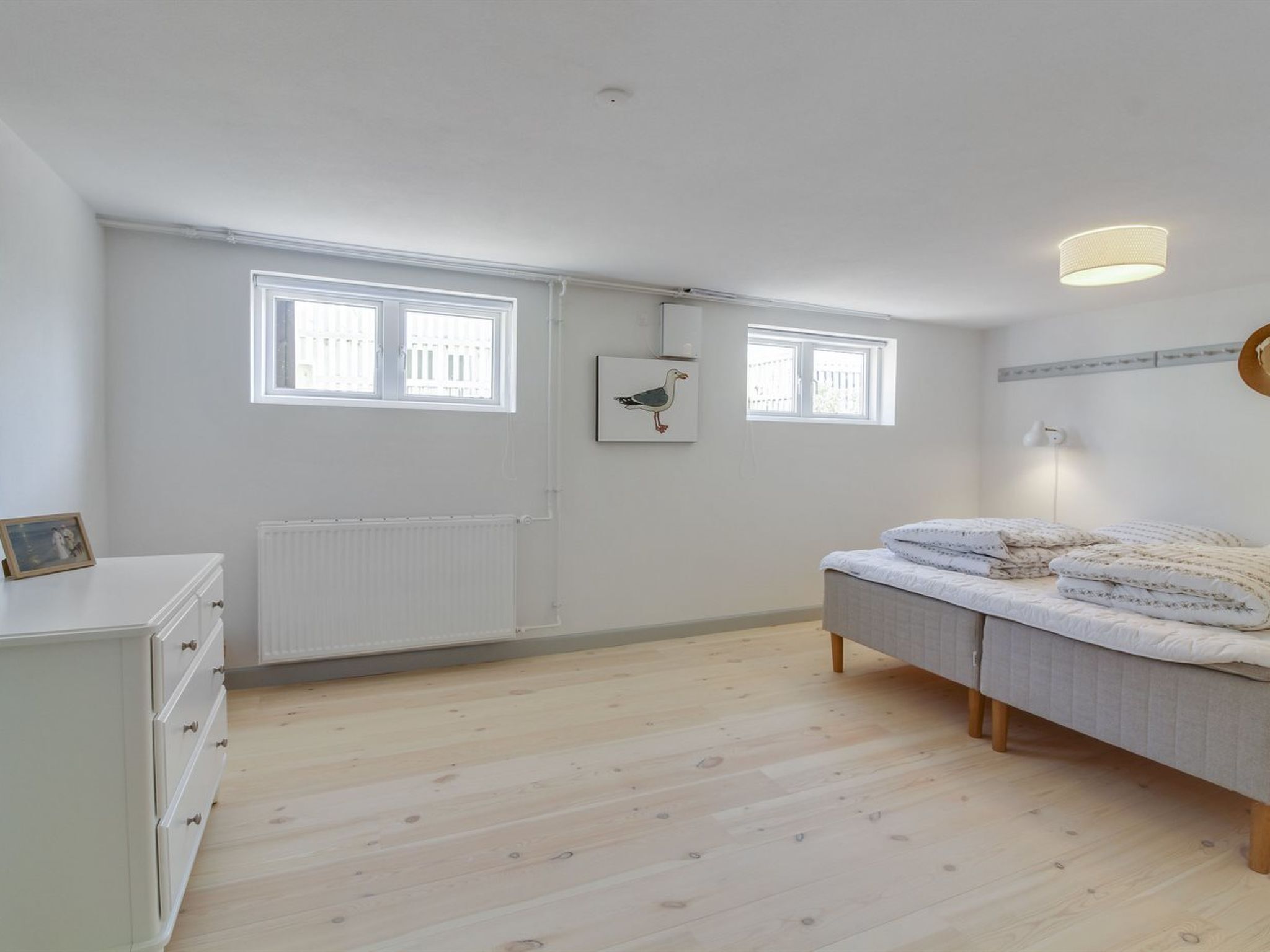 Ein Schlafzimmer mit einem Bett, einem Schminktisch, zwei Fenstern, einer Heizung und einer Wandleuchte.