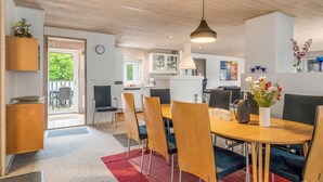 A modern kitchen with wooden cabinets, a dining area with a round table and chairs, and a visible clock on the wall.