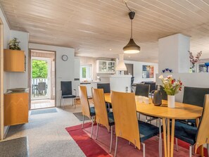 Una cocina moderna con armarios de madera, un comedor con una mesa redonda y sillas, y un reloj visible en la pared.