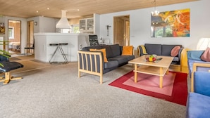A modern living room with a sofa, armchair, and coffee table, a kitchen area, and a dining space.