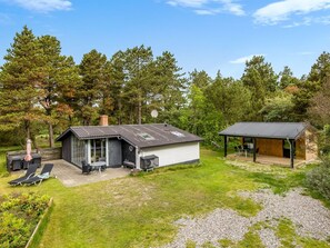 Une maison moderne dotée d’un patio, d’un espace extérieur aménagé et couvert, et d’une pelouse bien entretenue.