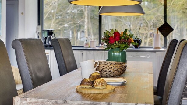 Ein Essbereich mit Holztisch, Ledersesseln, einer Blumenvase und einer Kaffeemaschine.