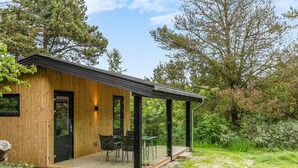 Eine moderne Holzblaus mit einer Terrasse, einem überdachten Außenbereich zum Sitzen und Blick auf den umliegenden Wald.