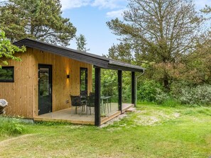 A modern wooden cabin with a deck, a covered outdoor seating area, and a view of the surrounding forest.