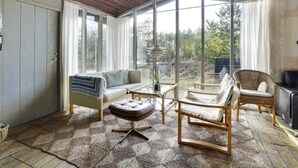 Ein gemütliches Zimmer mit Holzbalkendecke, einem großen Fenster, einem Sofa, einem Sessel und einem kleinen Tisch.