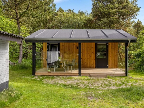 A modern house with a wooden exterior, a glass door, and a small patio with a table and chairs.