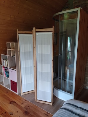 Una habitación con suelo de madera, una cama, un ventanal corredero y una estantería con libros y objetos decorativos.