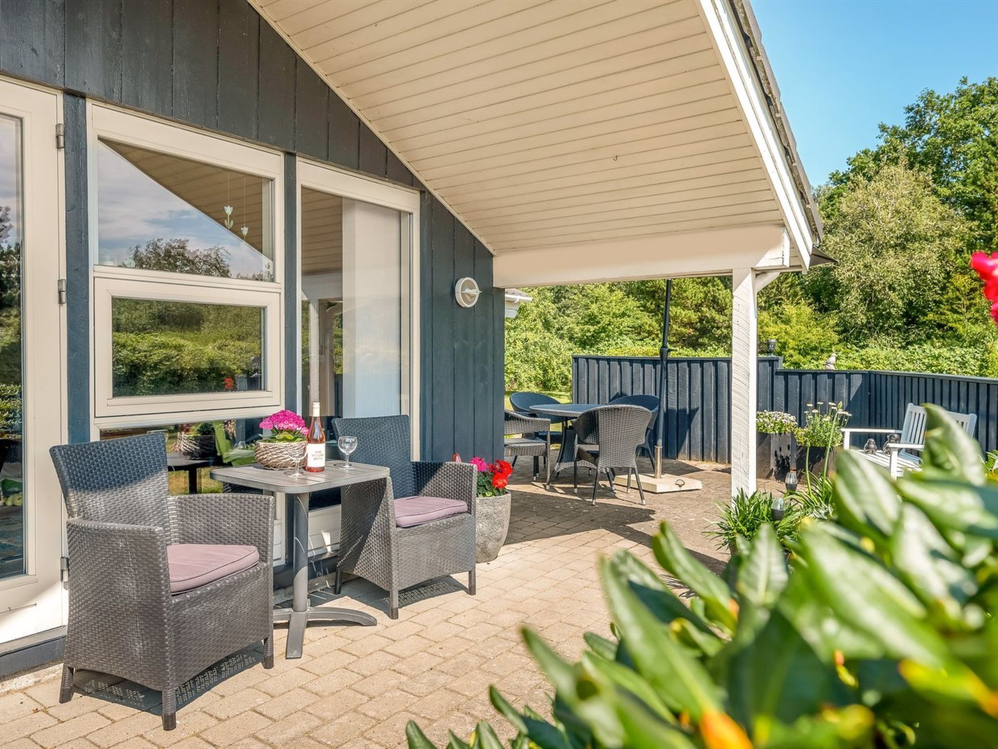 Un espace extérieur aménagé en terrasse, avec des meubles en osier, une table sur laquelle se trouvent une bouteille et un verre, et une vue sur la verdure.