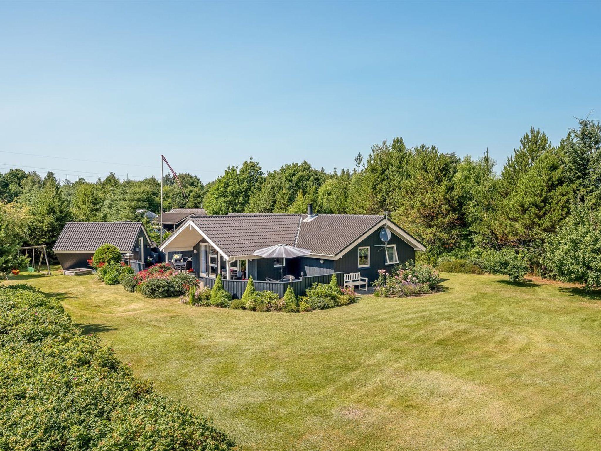 A two-story house with a covered patio, a fenced yard, and a wooded backdrop.