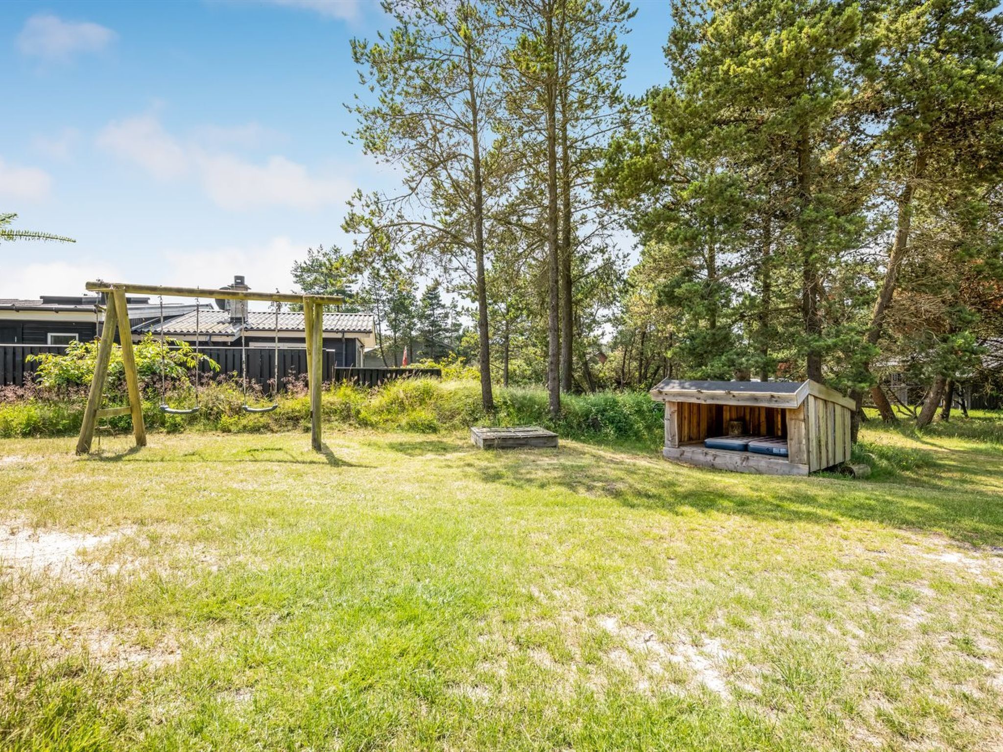 A backyard with a swing set, a wooden playhouse, and a small shed.