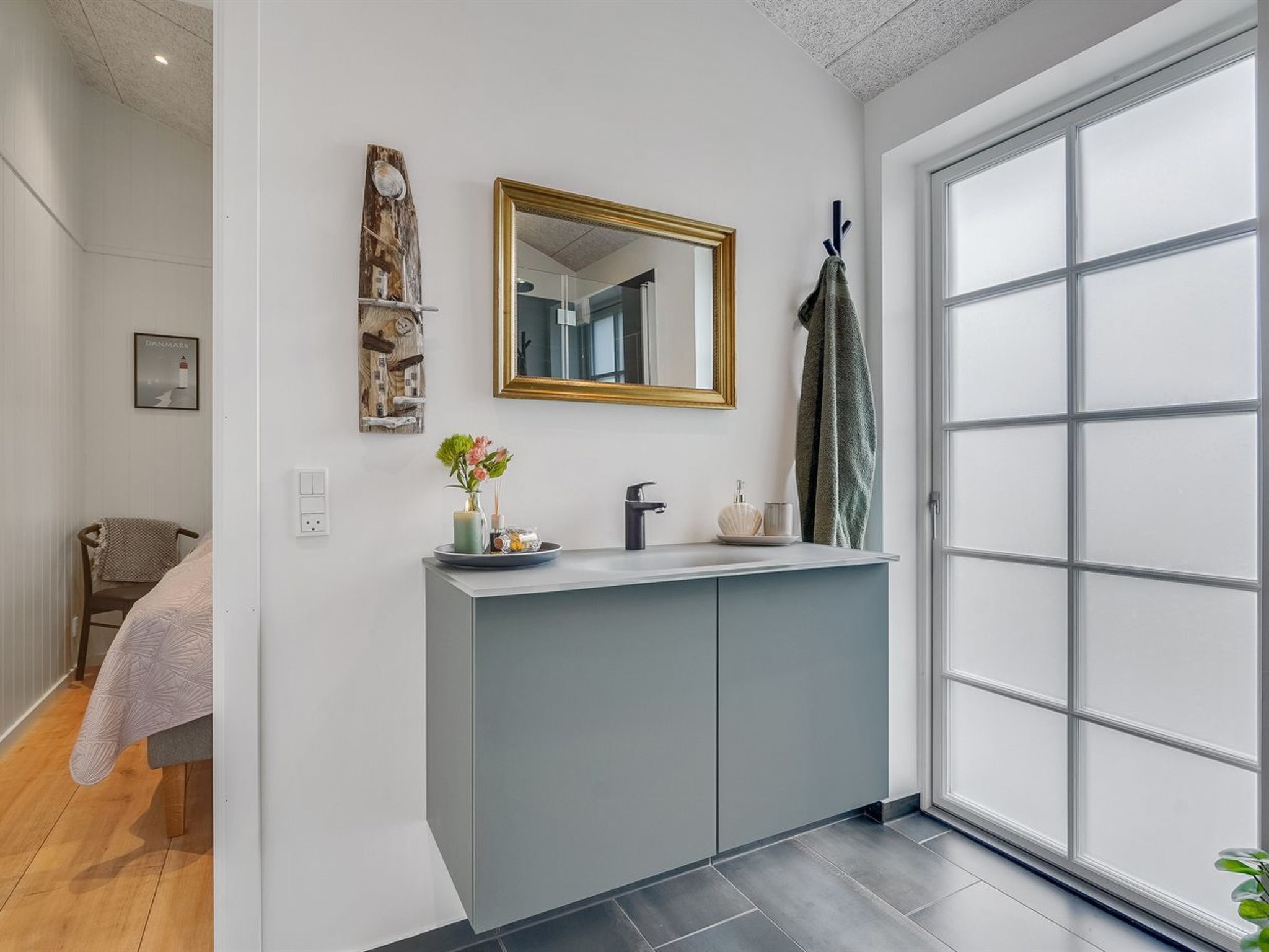 Un baño moderno con un tocador gris, un espejo grande y un ventanal con paneles de vidrio esmerilado.