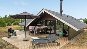 Een modern terras buiten met een barbecue, lounge stoelen en een overdekte eethoek.