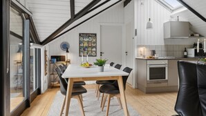 Een moderne keuken met witte kastjes, een eethoek met een witte tafel en zwarte stoelen, en een dakraam erboven.