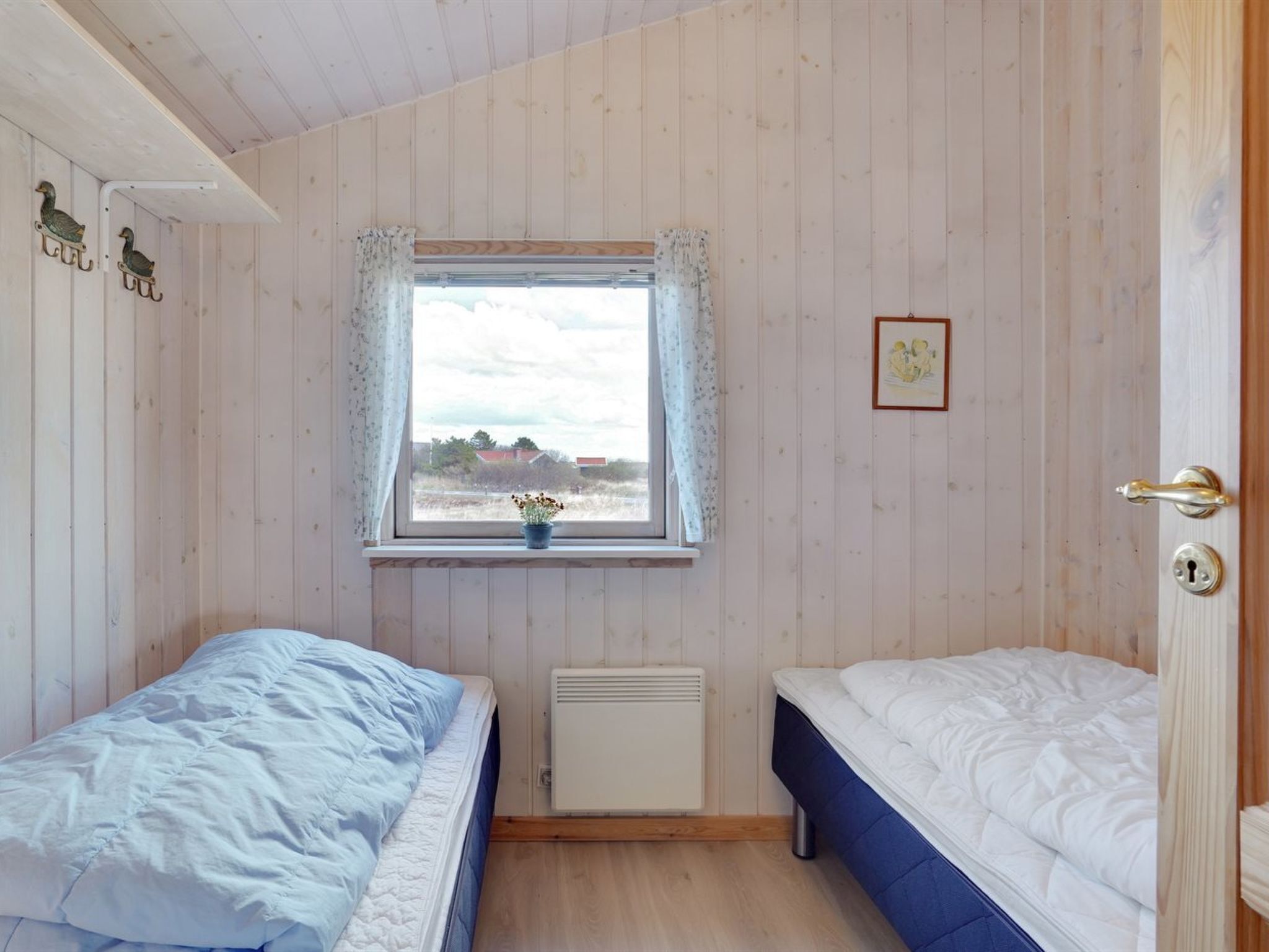 A small, single-room accommodation with two beds, a window with a view, and a radiator.
