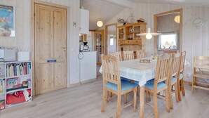 Une pièce aux murs lambrés, comprenant une table à manger, des chaises, un coin cuisine et une bibliothèque.