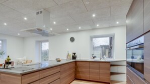 A modern kitchen with a large island, wooden cabinets, a built-in oven, and a window providing a view of the outside.