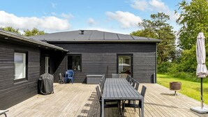 A modern house with a deck, a dining table, and outdoor furniture.