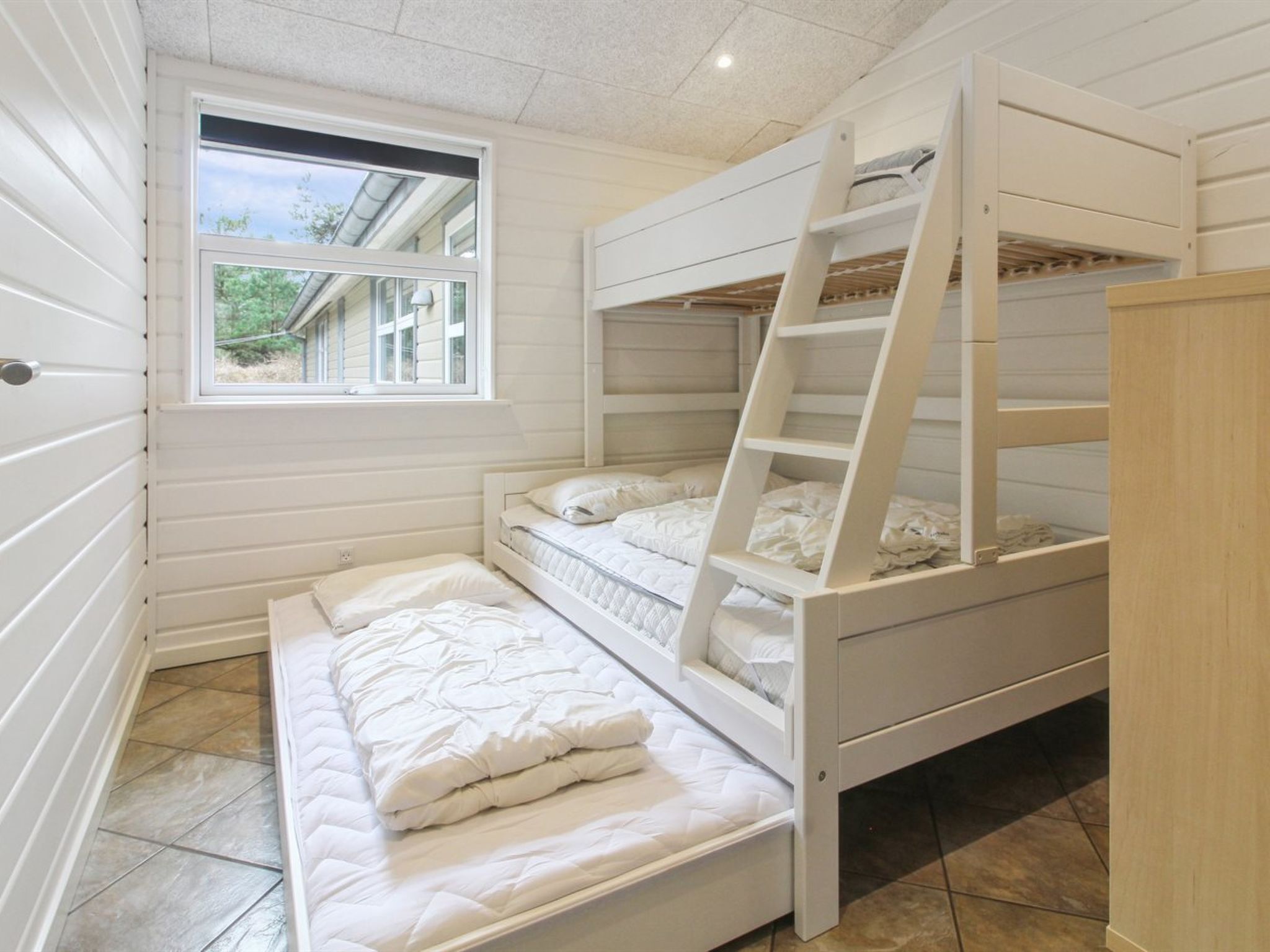 Une chambre avec un lit superposé, une fenêtre, une échelle et une armoire en bois.