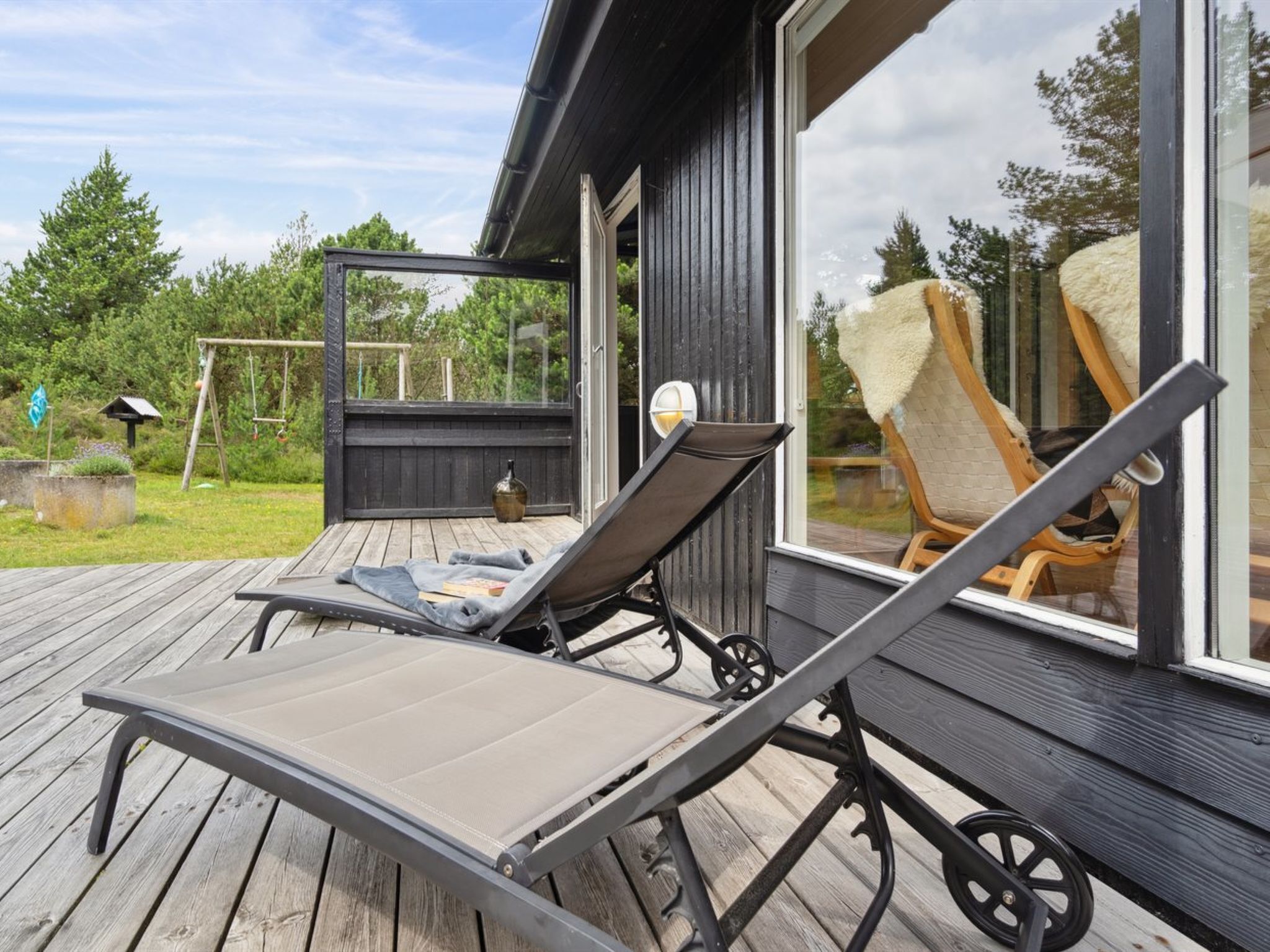A wooden deck with two sun loungers and a swing set.