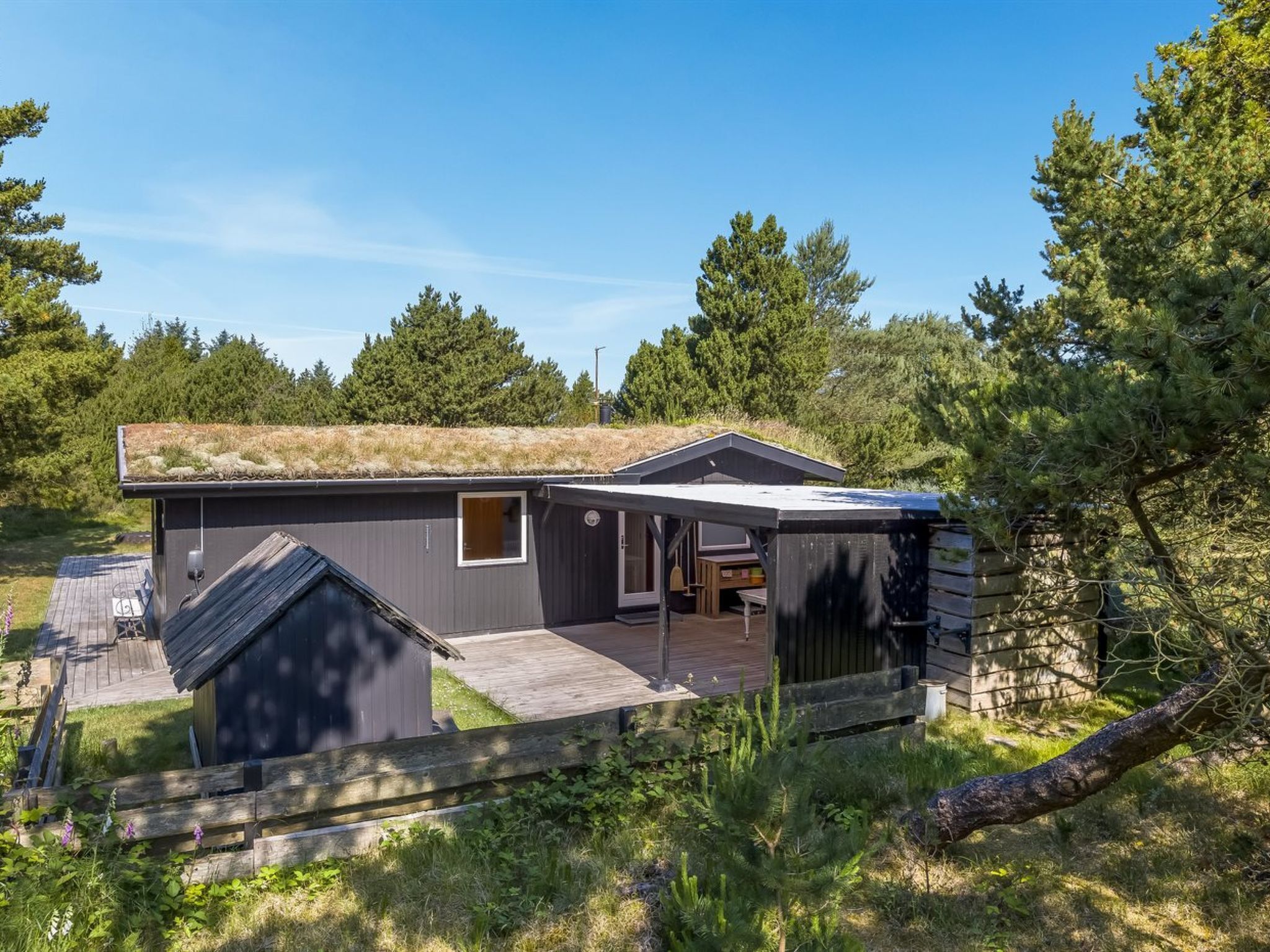 Ein modernes Haus mit geneigtem Dach, einer kleinen Veranda und einer Holzterrasse.