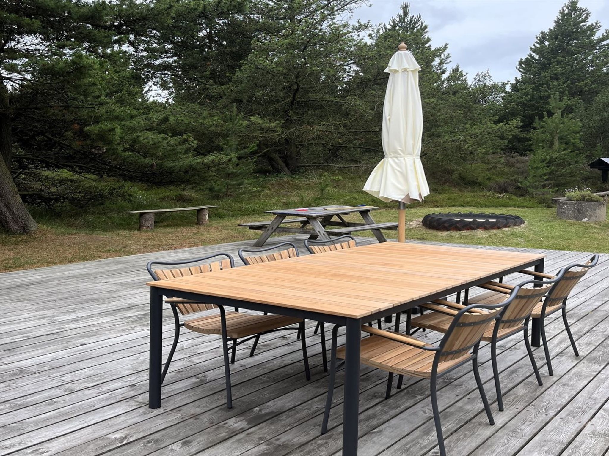 Une terrasse en bois avec une table de pique-nique, des chaises et un parasol blanc.
