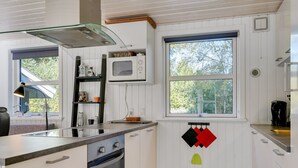 Uma cozinha moderna com armários brancos, forno embutido, micro-ondas e uma janela com vista para árvores.