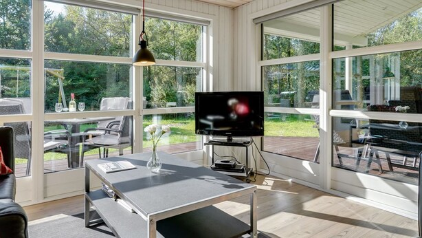 Uma sala de estar moderna com grandes janelas, uma TV de tela plana e uma área de jantar com mobiliário para área externa.