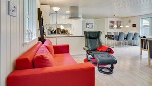 Uma sala de estar moderna com um sofá vermelho, uma cadeira preta e um espaço de jantar com mesa e cadeiras.