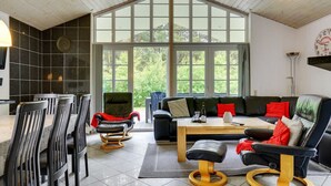 A spacious living area with a large window, a black leather sofa, a dining table, and a black leather chair.