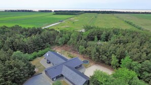 A house with a large driveway, surrounded by dense forest and open fields.