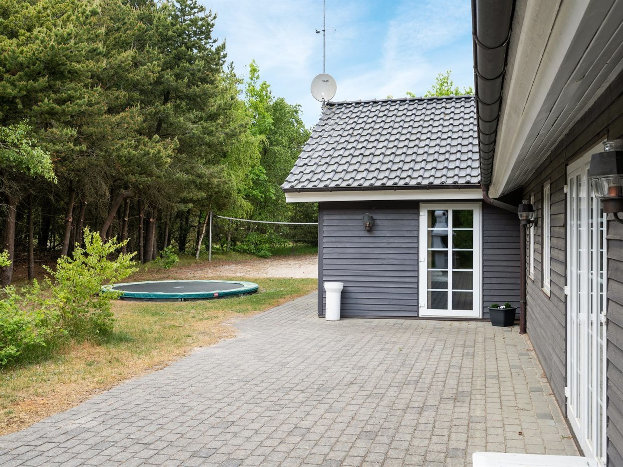 A house with a tiled roof, a satellite dish, a trampoline, and a paved driveway.