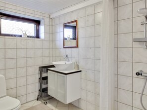 A bathroom with white tiles, a window, a sink with a mirror above it, and a shower.