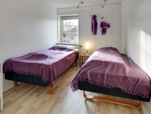 A room with two beds, a window, a lamp, and a painting on the wall.