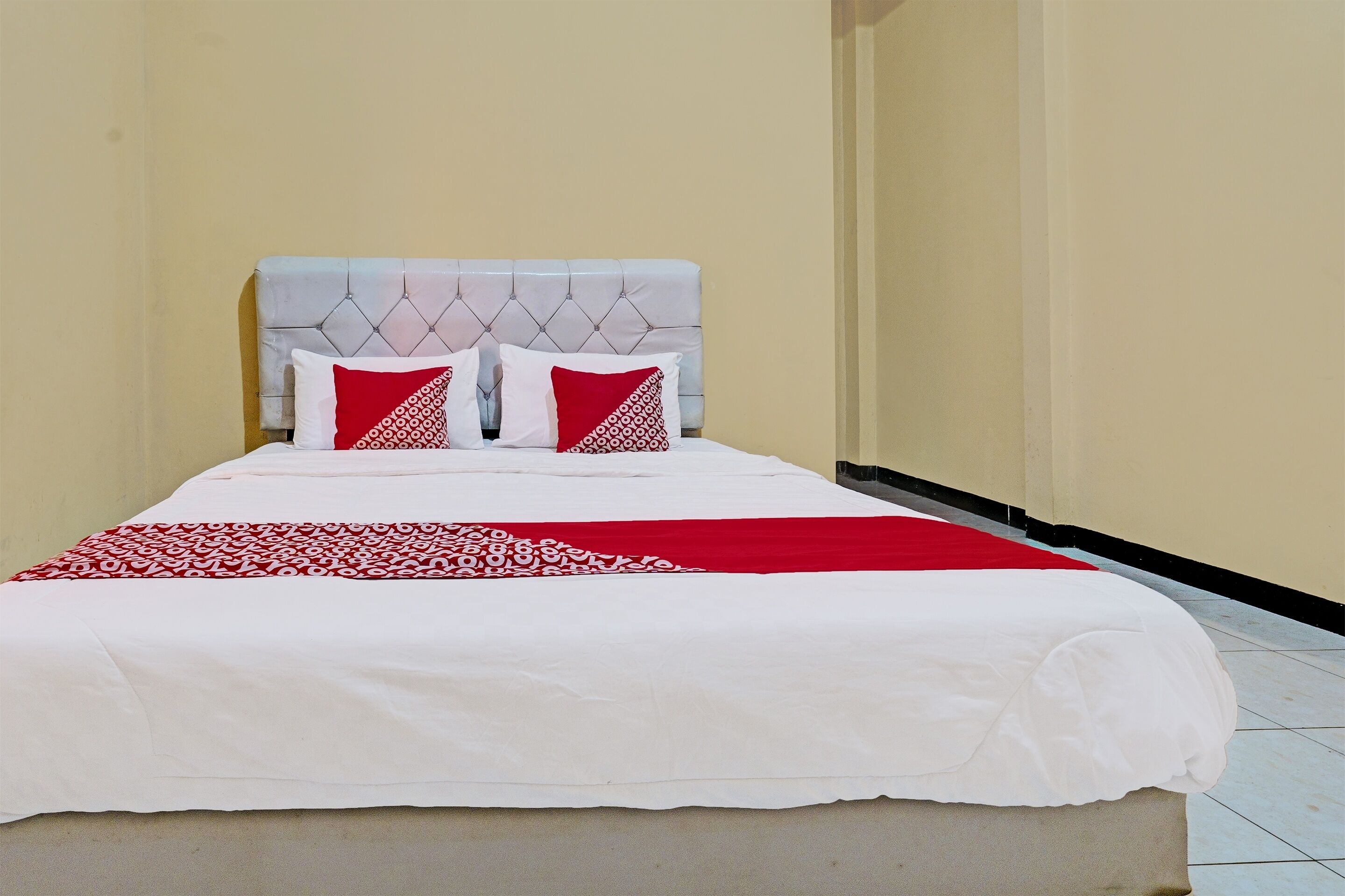A neatly made bed with a white and red bedspread, two pillows with a red and white pattern, and a tufted headboard.