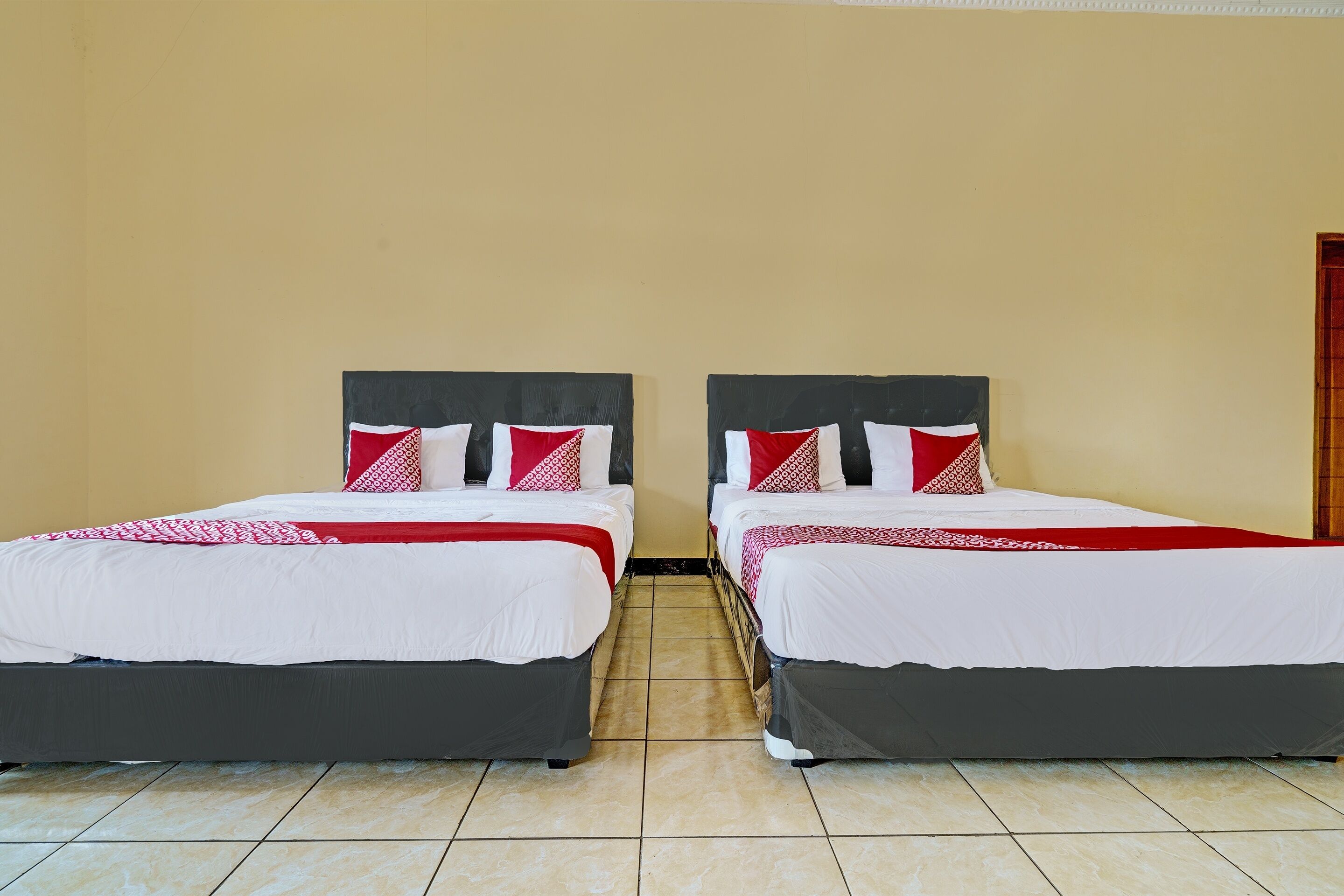 Habitación de hotel con dos camas, cada una con cabecera negra y ropa de cama blanca, con almohadas estampadas en rojo y blanco.