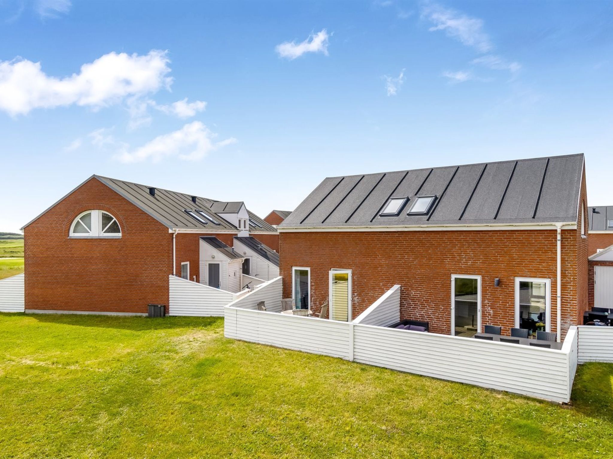 A row of modern brick houses with sloped roofs and skylights, connected by a white fence.