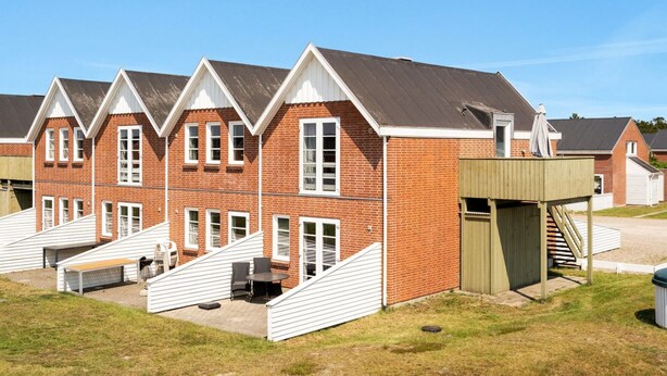 A row of brick houses with white trim, each featuring a small deck and a covered outdoor seating area.