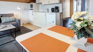 A compact living space with a kitchenette, a sofa, a dining table with orange placemats, and a decorative plant.