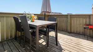 A wooden deck with a table and chairs, an umbrella, and a barbecue grill.
