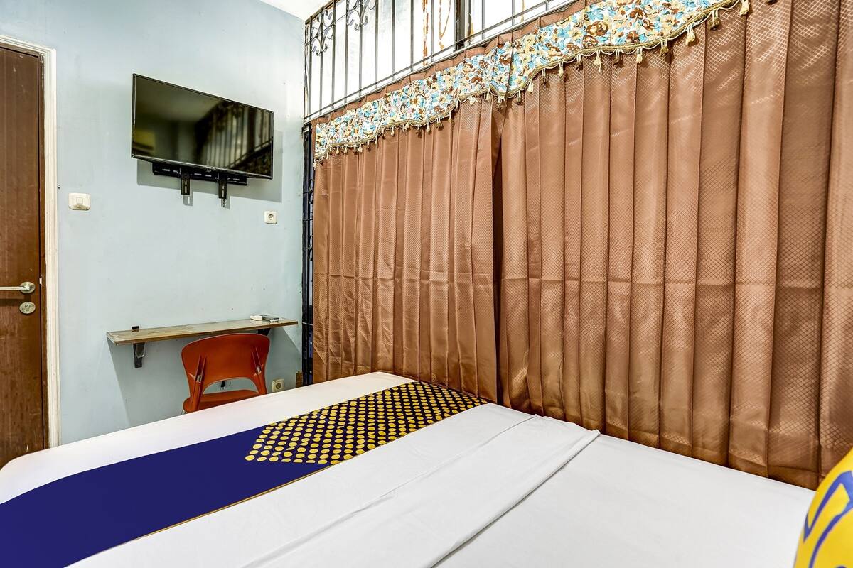 Ein Schlafzimmer mit einem Bett, einem an der Wand befestigten Fernseher, einem Vorhang und einem Sessel.