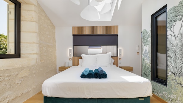A modern bedroom with a large bed, wooden headboard, and a view of trees through a window.
