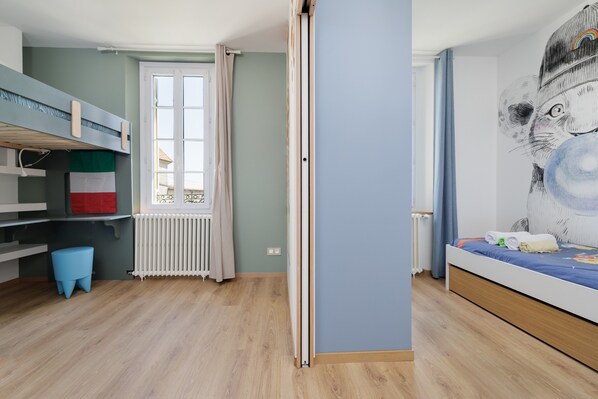 Una habitación con literas, un radiador, una ventana con cortinas y un mural en la pared.