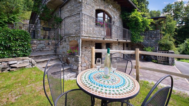 Ein Steinhaus mit Balkon, Sitzgelegenheit im Freien und Holzzaun.