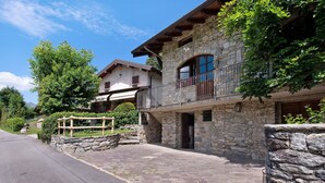 Ein Steinhaus mit Balkon, einer gepflasterten Auffahrt und einer Holzpergola mit hängenden Pflanzen.
