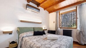 Ein Schlafzimmer mit Bett, Nachttischen, einem Fenster mit Vorhängen, einem Heizkörper und einem Deckenventilator.