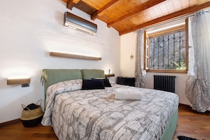 Une chambre à coucher comprenant un lit, des tables de chevet, une fenêtre avec des rideaux, un radiateur et un ventilateur de plafond.