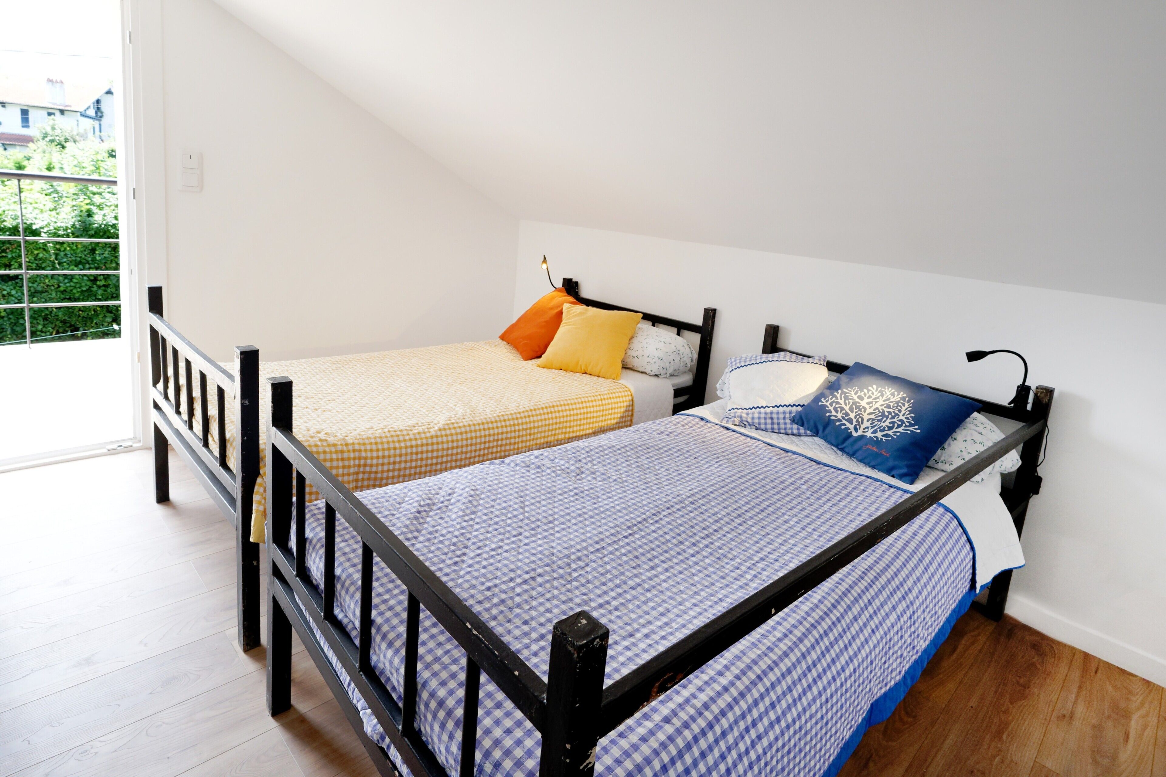 Twee bedden met zwarte frames, een raam met uitzicht en een deur.